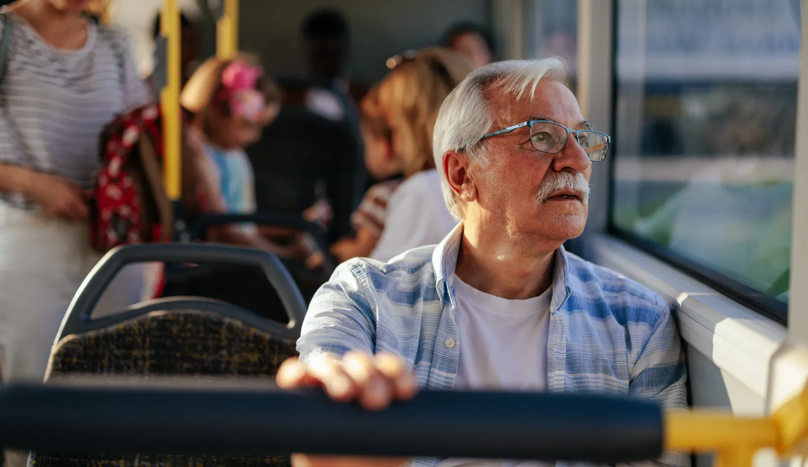 An elderly man is in a public transport bus sitting and looking through the window.