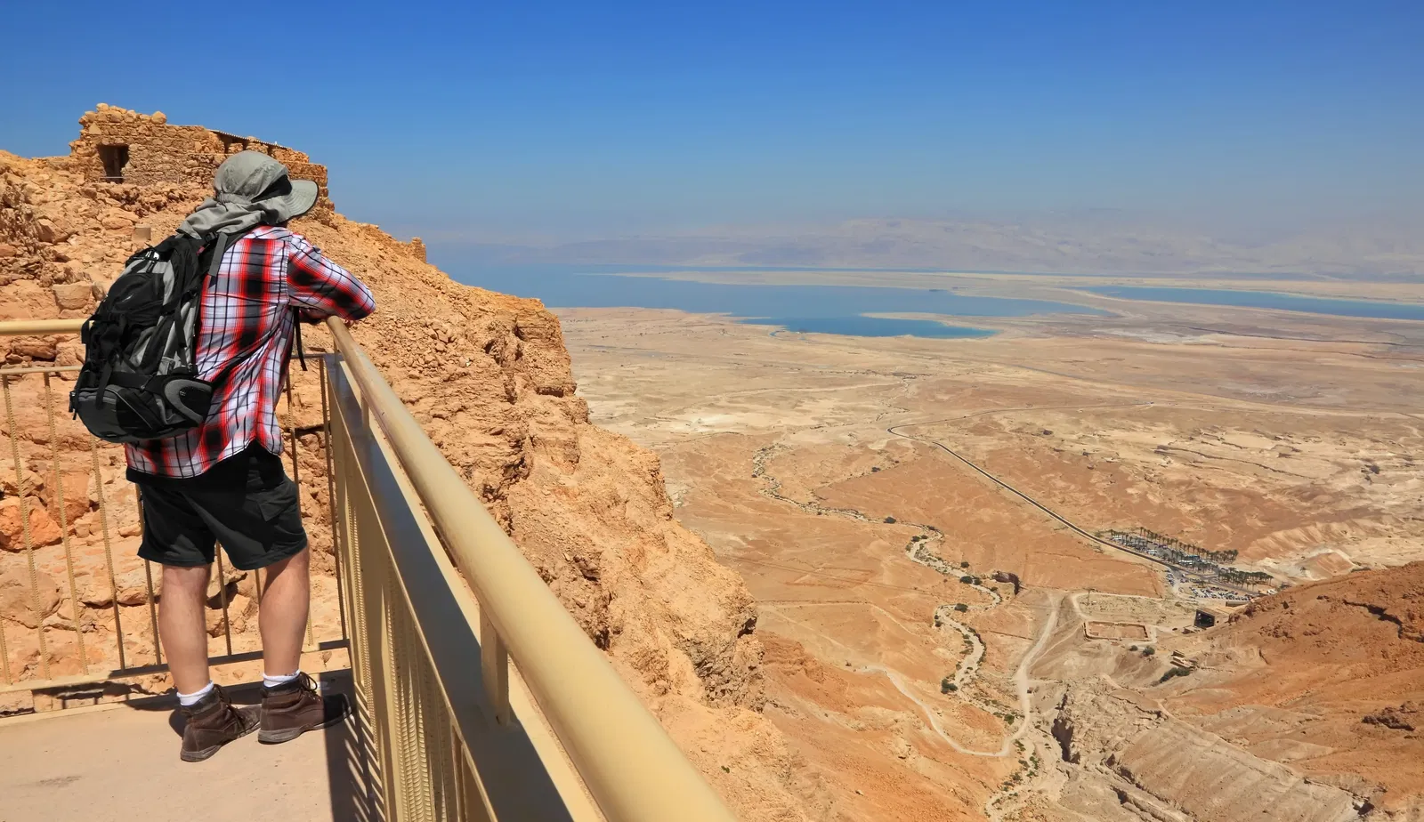 A man with a hat looking at the Dead Sea from a balcony.