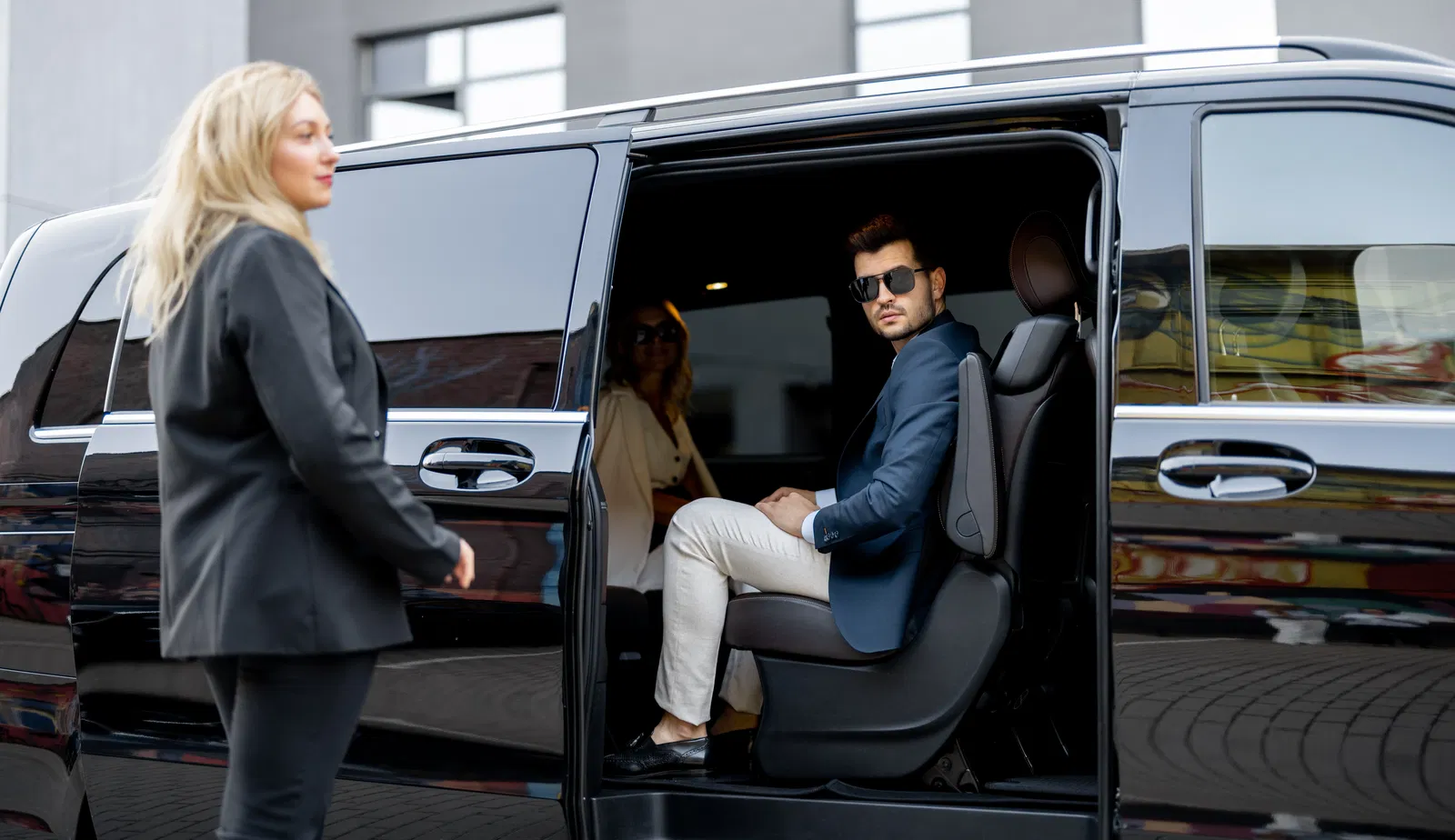 A man in a suit and sunglasses sitting in a black luxurious minibus.